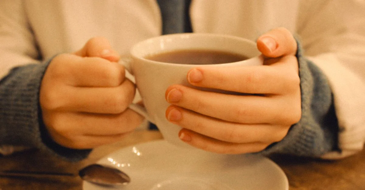 Gros plan sur des mains tenant une tasse de café fumante lors d'une journée confortable à l'intérieur, parfait pour des moments chaleureux.