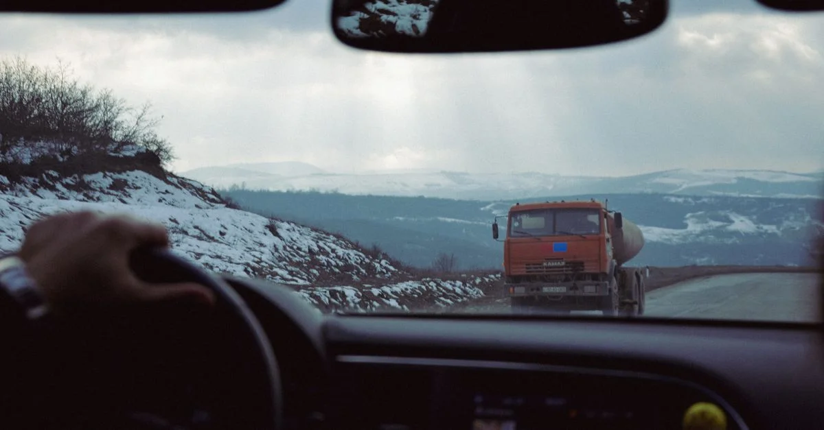 Vue de l'intérieur d'une voiture s'approchant d'un camion sur une route de montagne enneigée.