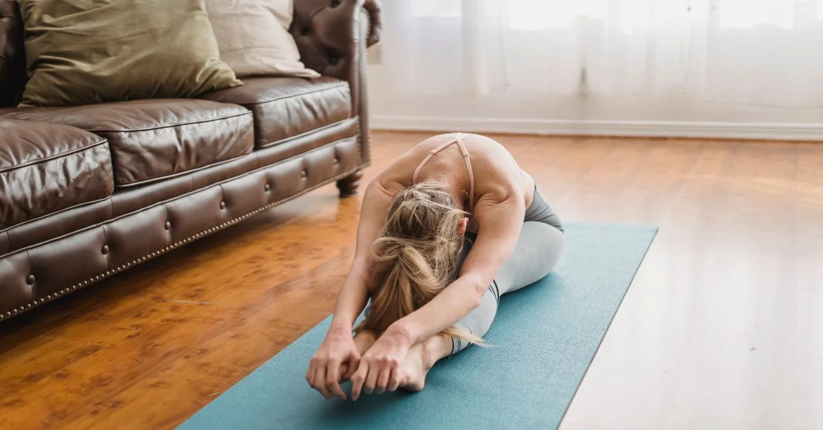 Femme faisant du yoga dans un salon, se concentrant sur une posture de flexion avant assise pour le bien-être.