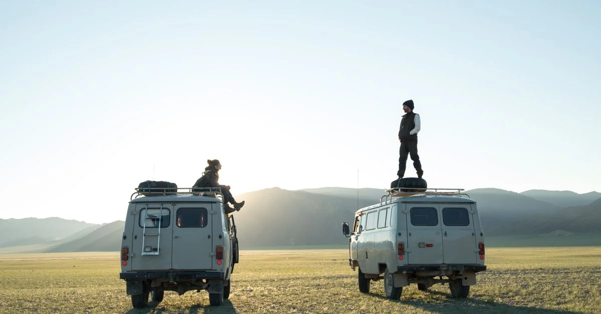 Deux personnes explorant une vallée montagneuse pittoresque avec des vans au lever du soleil, incarnant l'envie de voyager et l'aventure.