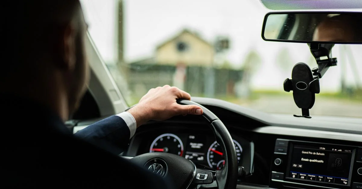 Homme d'affaires en costume conduisant une voiture, se concentrant sur le volant et le tableau de bord.