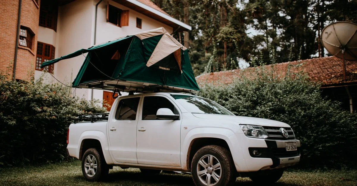Véhicule utilitaire blanc avec tente de toit garé près d'une maison, idéal pour des thèmes de camping et de voyage.