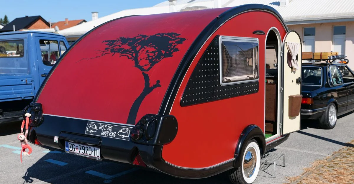Une remorque rouge vibrante dans un parking urbain avec un design personnalisé, mettant en valeur un style de vie moderne de camping.