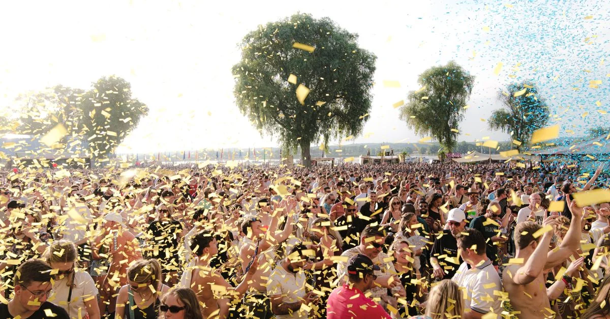 Une foule animée profitant d'un festival de musique en plein air avec des confettis sous un ciel ensoleillé.