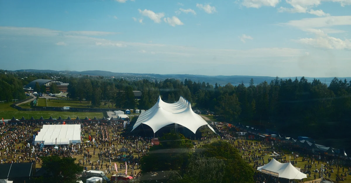 Grande foule lors d'un festival de musique en plein air avec des tentes et un ciel bleu.