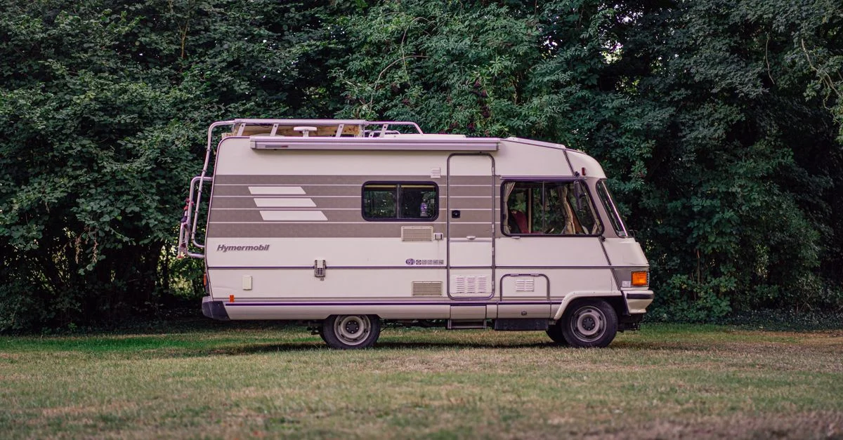 Un classique camping-car Hymermobil garé parmi des arbres verts et de l'herbe, parfait pour explorer la nature.