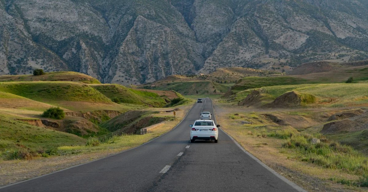 Vue pittoresque d'une autoroute avec des voitures entourées de collines verdoyantes et de majestueuses montagnes en été.