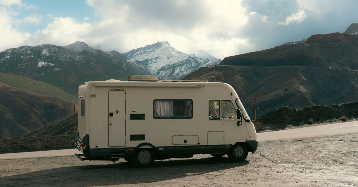 Camping-car garé au bord de la route avec un superbe décor de montagnes enneigées, idéal pour les thèmes de voyage et d'aventure.