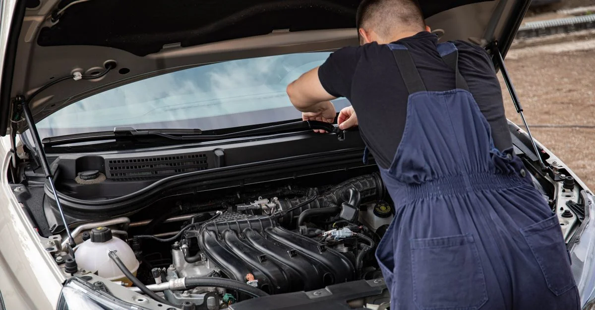 Un mécanicien en salopette bleue travaillant sur le moteur d'une voiture dans le cadre d'une routine d'entretien.