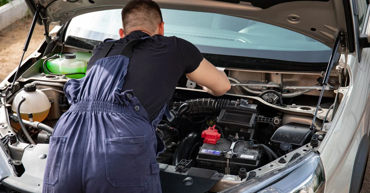 Mécanicien en salopette travaillant sur un moteur de voiture en extérieur, mettant en avant ses compétences en réparation de véhicules.